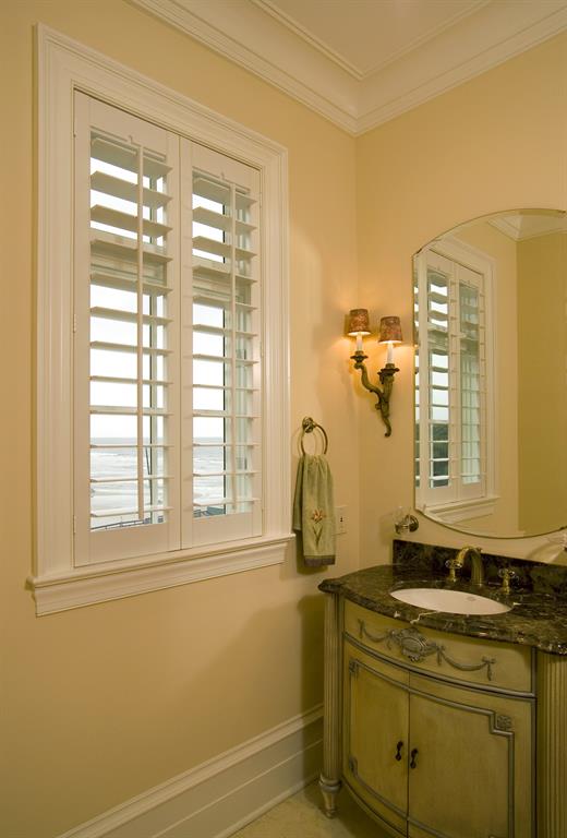 Plantation shutters in a light bathroom give a view of the ocean